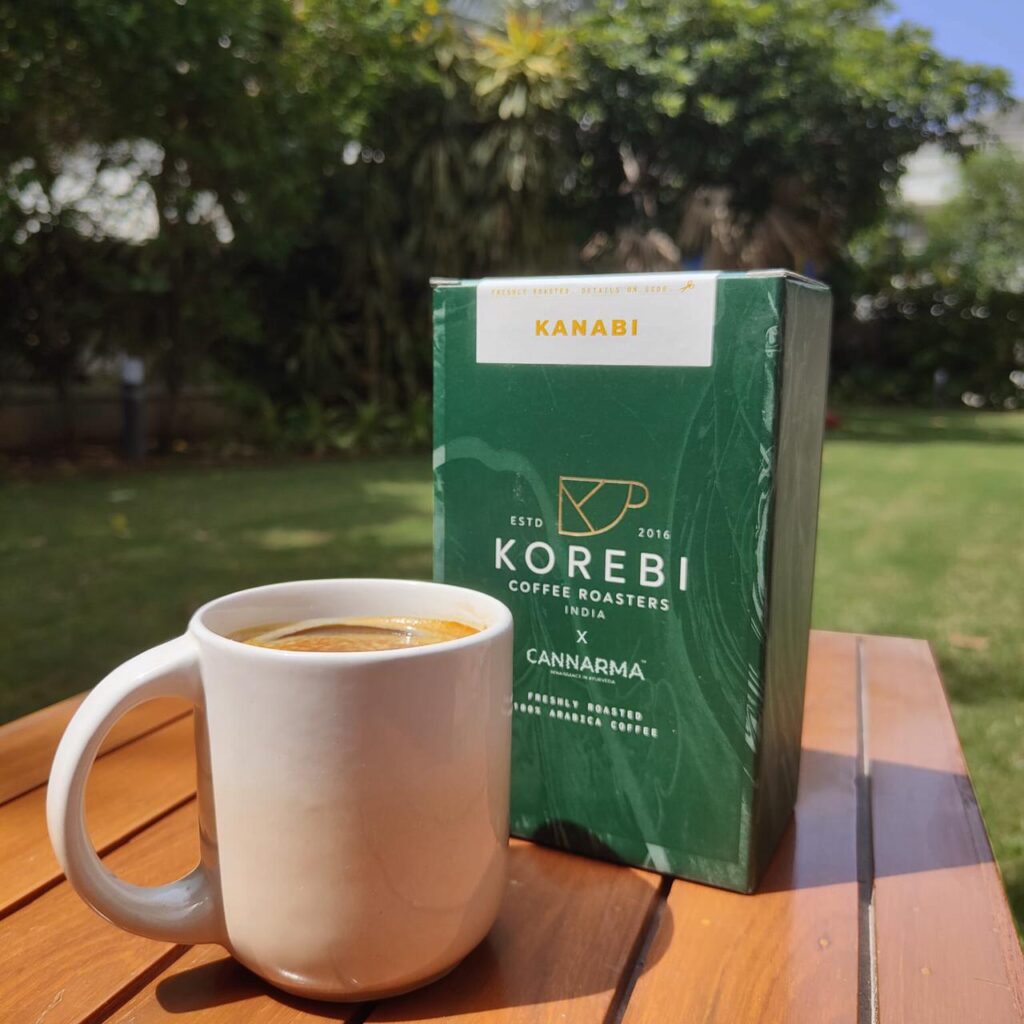 Cannarma Kanabi Infused Coffee in Green Box with a Cup of Brewed Coffee on a Wooden Table
