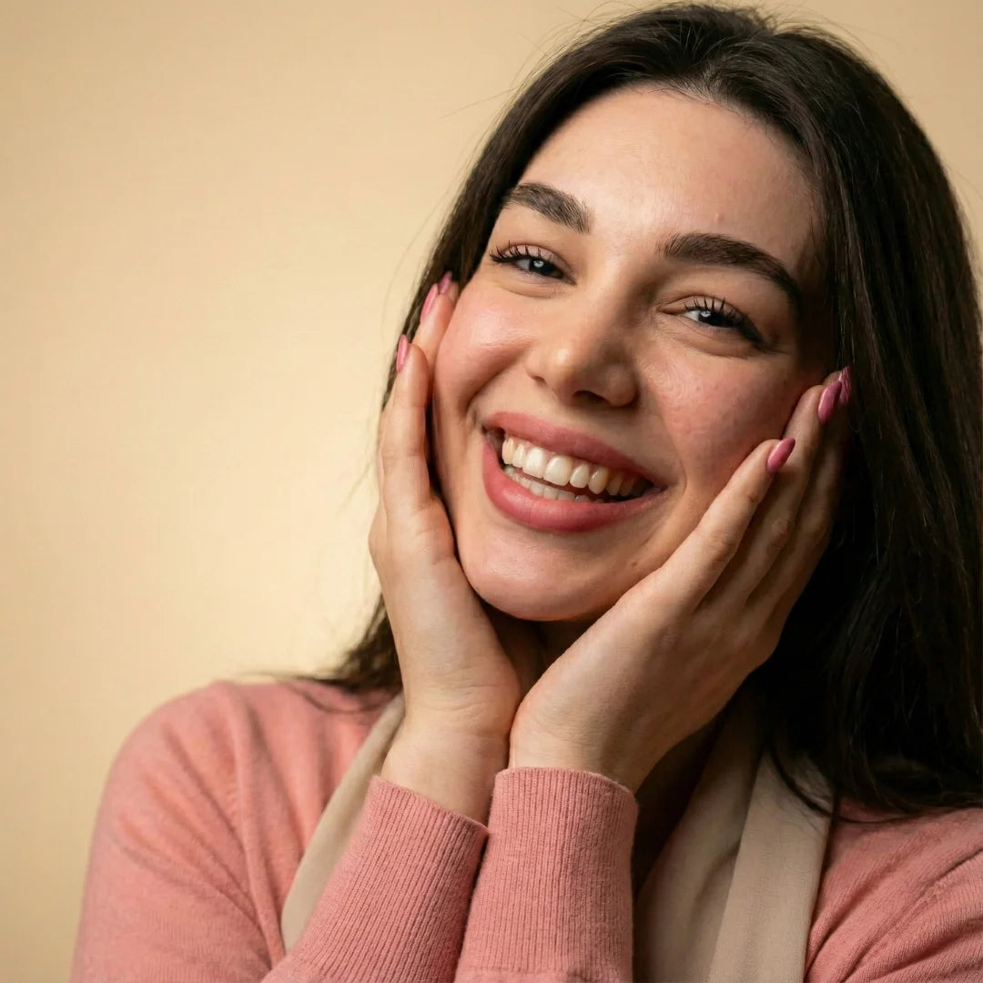 Woman smiling with hands on her cheeks against a beige background